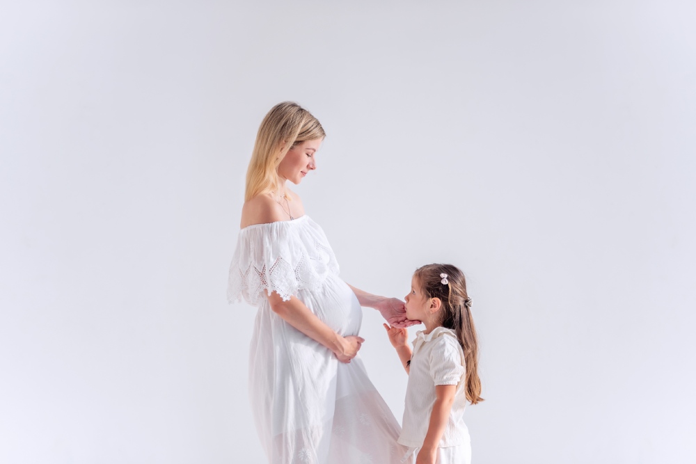A little girl and her pregnant mother, both wearing white